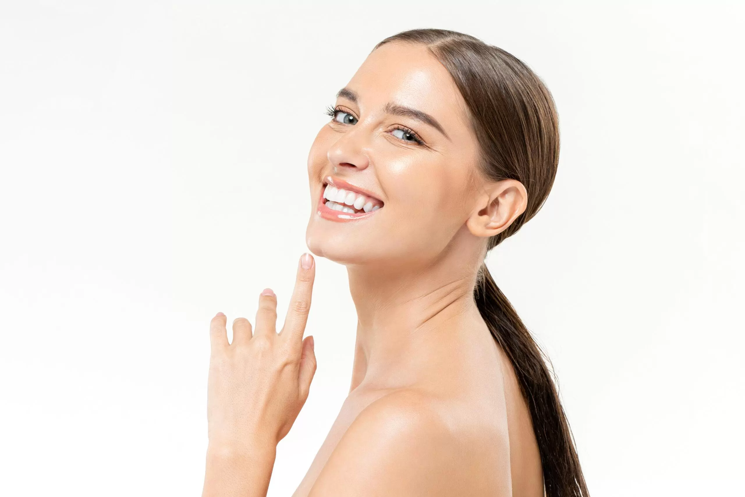 Beauty portrait of cheerful Caucasian female with with finger at chin on white isolated background in light studio faccette dentali in ceramica